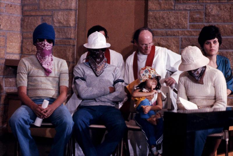 Photo of Rev. Arthur Lloyd and Laurie Lemel sitting behind four El Salvador refugees at St. Francis House, circa 1983